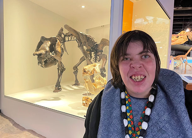 A woman stands in front of a museum display of a dinosaur skeleton, she is smiling