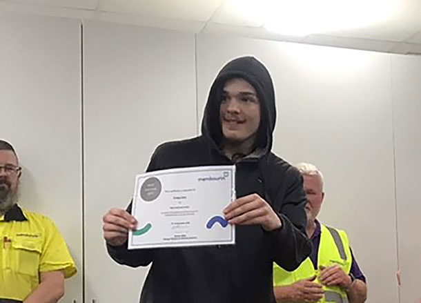 A person in a black hoodie smiles holding up a certificate