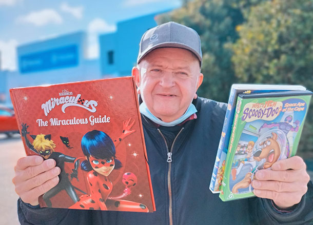 A man standing outside holds up a book and DVD 