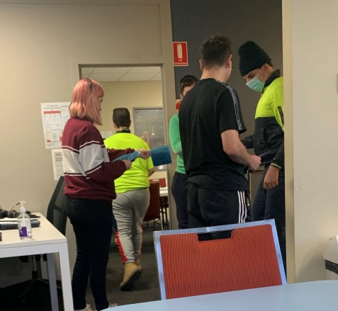 A group of SLES participants stand in a classroom, two are handing out flyers to the others