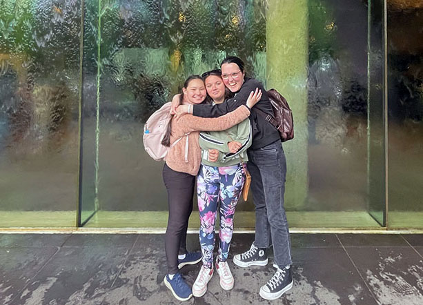 Cindy, Brooke and Shakaya have a group hug in front of the NGV waterwall