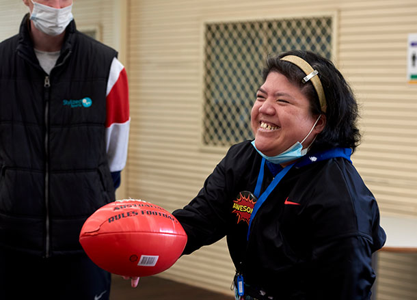 A woman is about to handball a red AFL football, she has a big smile