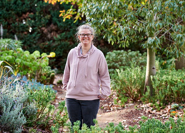 A person standing outside in a beautiful leafy garden, she is smiling