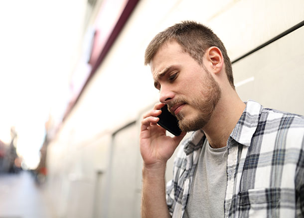 A man leans up against a wall holding a phone to his ear