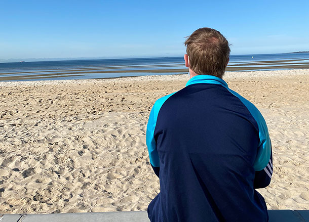 A man sits looking out at the beach