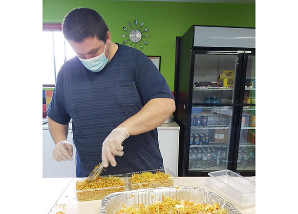 Daniel is using tongs to serve noodles from a large tray into plastic containers