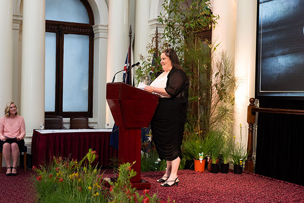 Dee-Jay stands at a podium making a speech