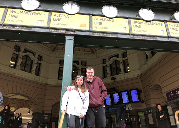 Two people stand underneath the clocks at Flinders Street Station