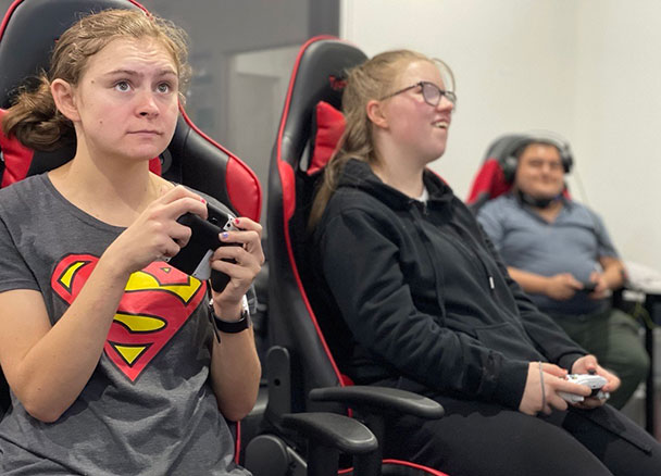 Three people in gaming chairs using handheld controllers