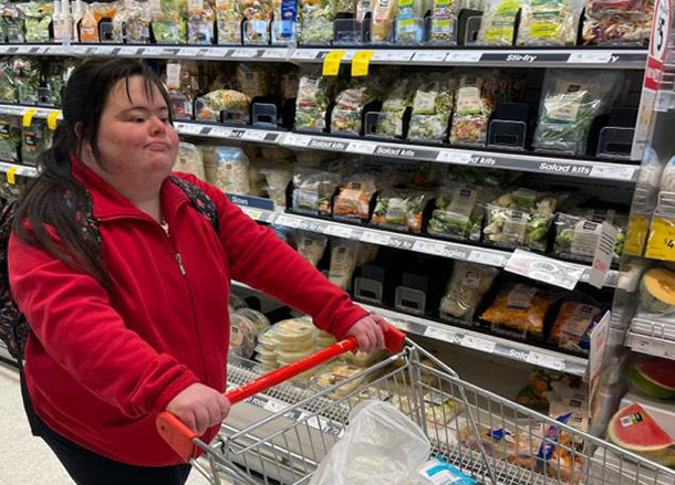 A woman pushes a shopping cart through the fresh food section of a supermarket