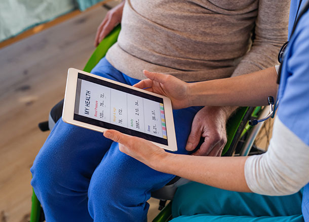 A person holds an iPad with medical information on it, showing a person in a wheelchair