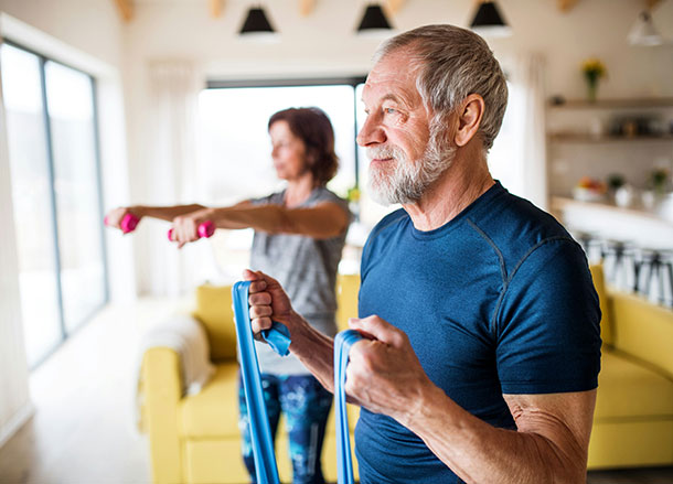 Two middle aged adults stand doing stretches in their living room