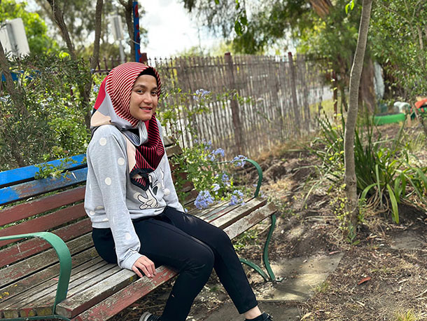 Imelda sits outside on a garden bench, she is smiling