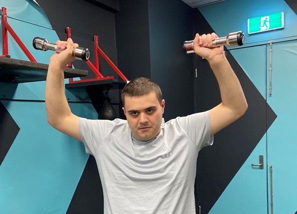 A man lifts two dumb bells above his head