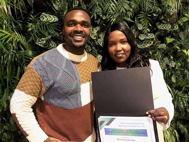 Marie stands holding her certificate, a man stands beside her smiling