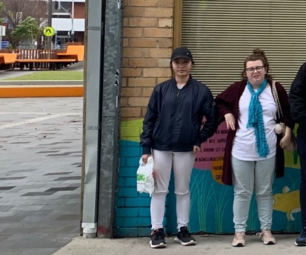 Monica and Caitlin are standing in the street against a brick wall