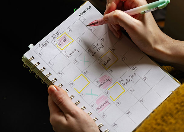 A holds a monthly planner in one hand, and is writing in it with the other hand