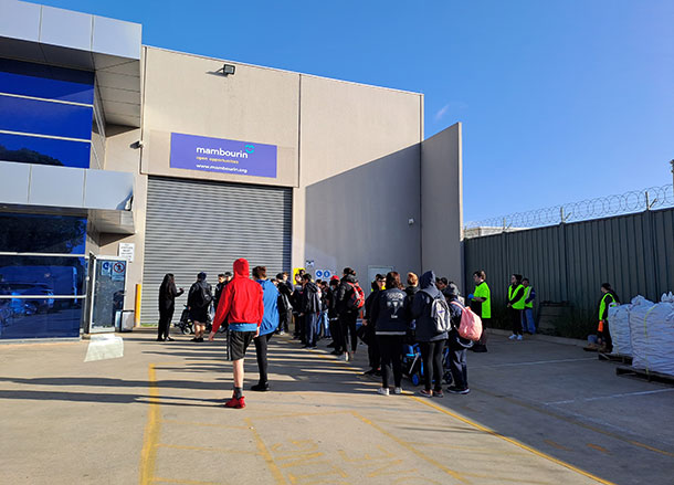 A large group of people form a queue in the Mambourin warehouse carpark