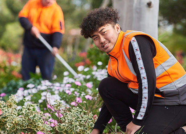 A young man in a high-vis vest is crouched down gardening