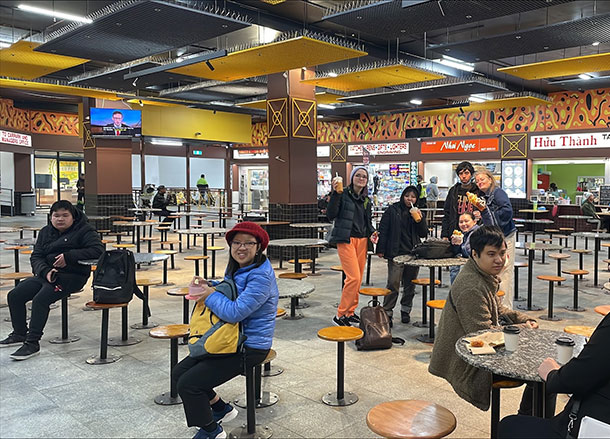 Ten people sit around in a food court with takeaway snacks, juices and coffees