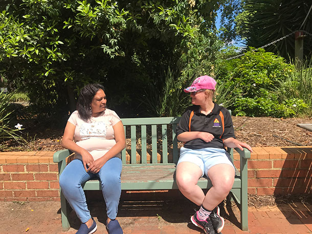 Khushboo and Sam sit outside on a park bench chatting