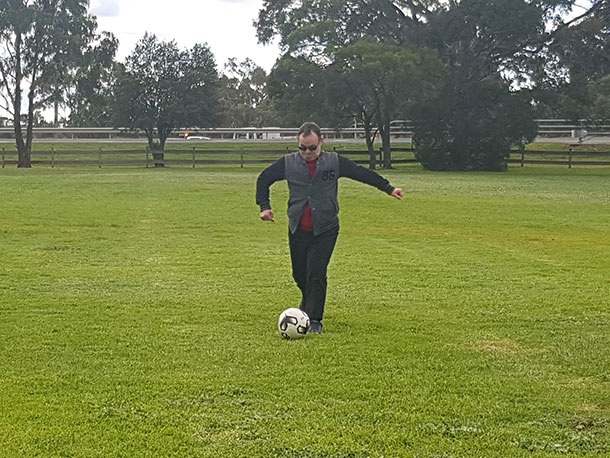 A person stands on a green oval about to kick a soccer ball