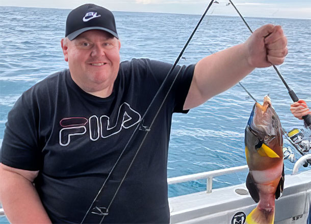 Steven is on a boat holding up a fish on a line, he is smiling