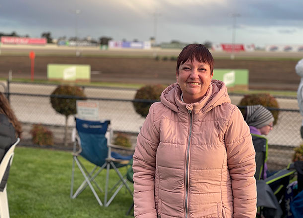 A woman stands in front of a horse racetrack at dusk