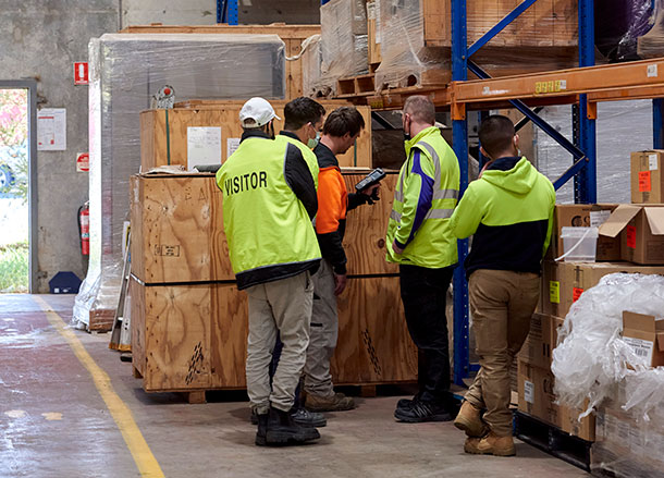 Five people in high vis stand around a pallet in a warehouse
