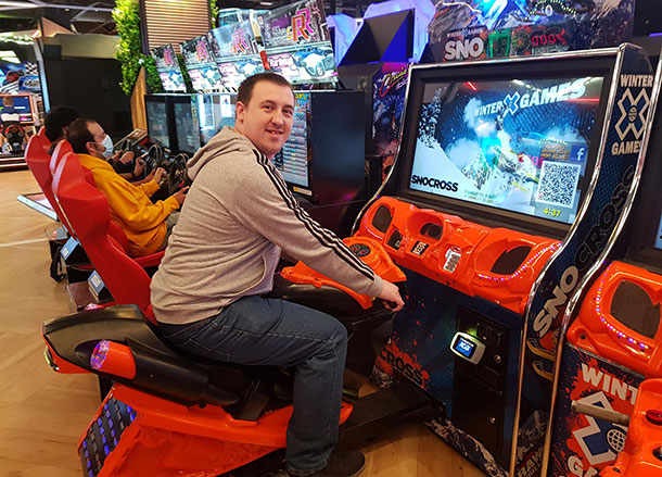 Samuel is riding a video game motorbike in an arcade