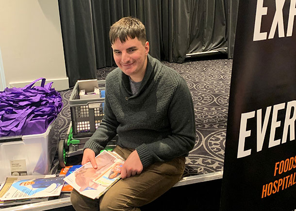 Tristan is sitting holding expo materials in his hands, he is smiling