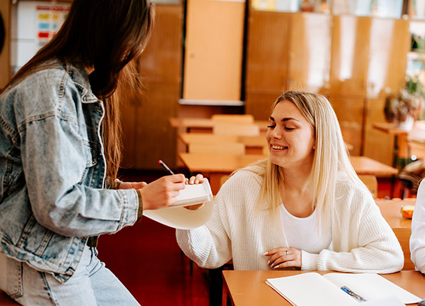 A woman takes a piece of paper from a woman sitting at a table