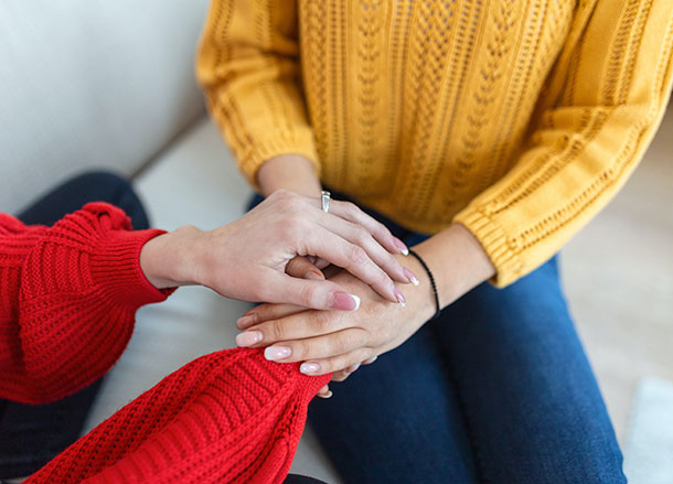 Two people are sitting, one person has placed their hands over the other person's hands