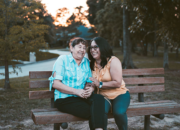 Two women sit close together on a park bench, they are laughing