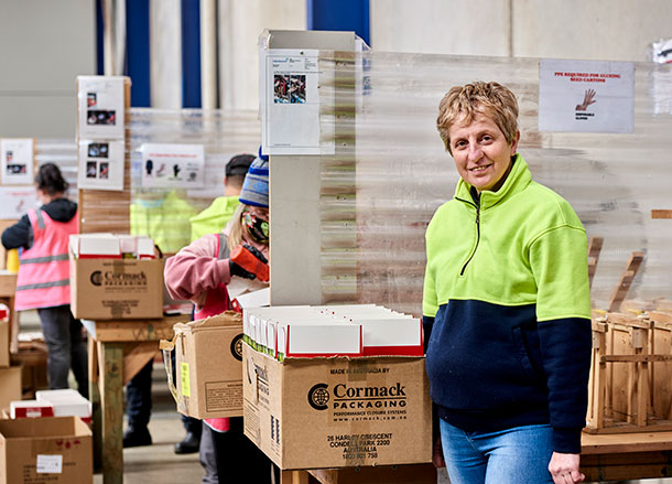 A woman is standing at a workstation, she is smiling, people are working at other stations behind her