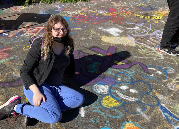 A person sitting on the ground outside, the concrete is covered in graffiti art
