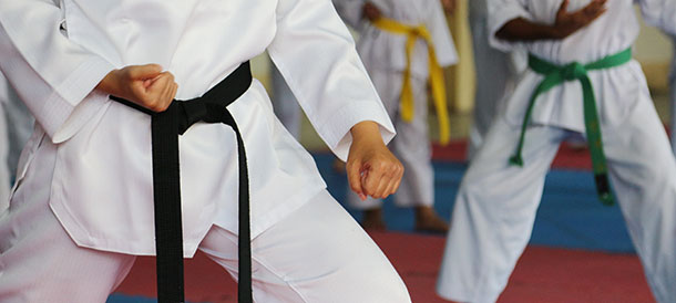 Torsos of 3 people in white taekwondo uniforms one had a black belt, one has a green belt and one has a yellow belt, they are in a taekwondo stance
